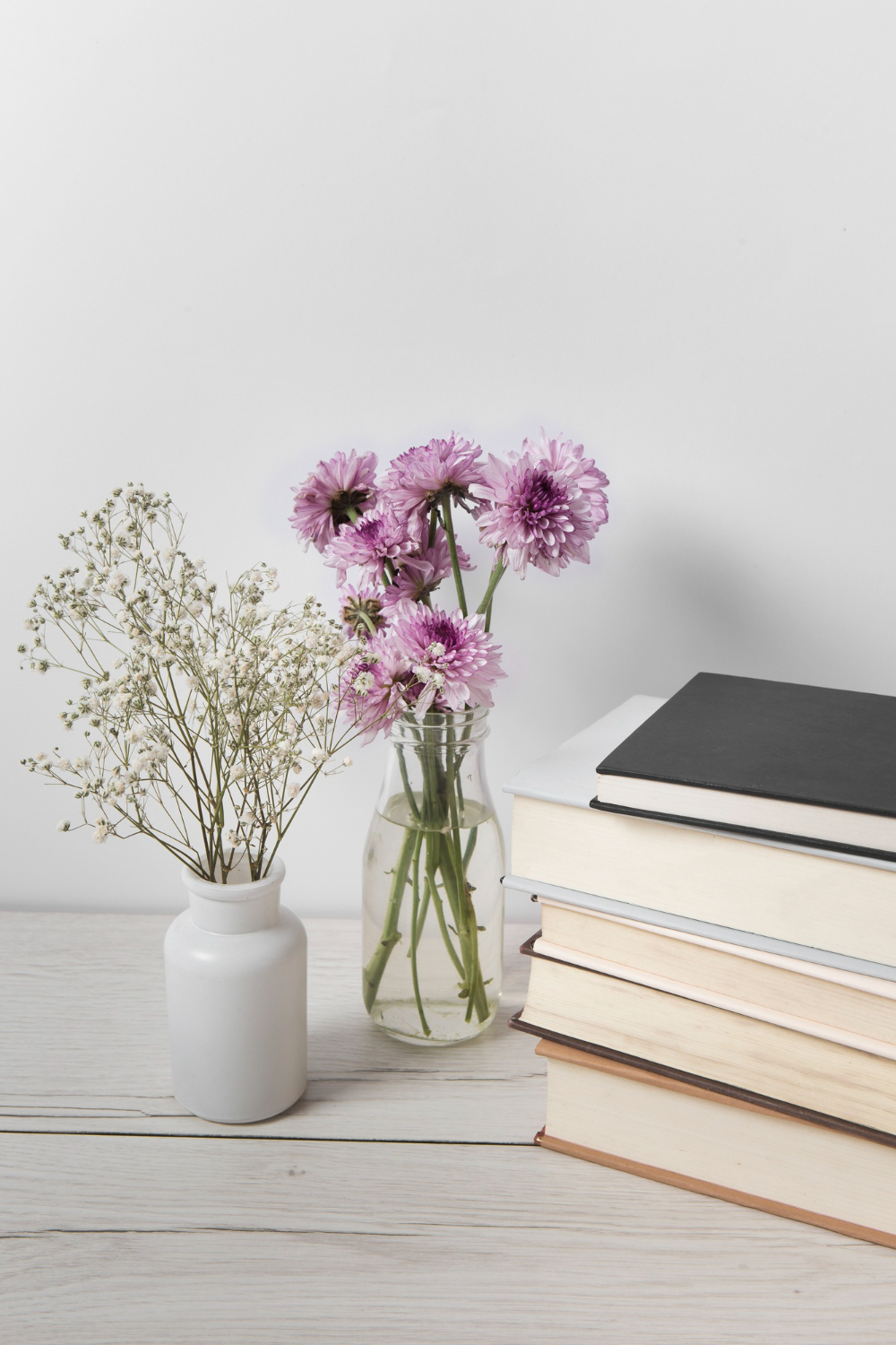Vaasje met paarse bloemen naast een stapel boeken